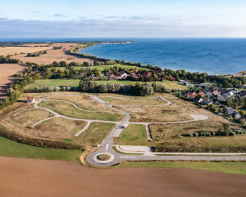 Luftaufnahme des Ferienparks Ostseeblick Wohlenberg: Im Vordergrund sind neu erschlossene Ferienhausgrundstücke der LGE zu sehen, eingebettet in eine grüne Küstenlandschaft mit Blick auf die Ostsee.