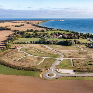 Luftaufnahme des Ferienparks Ostseeblick Wohlenberg: Im Vordergrund sind neu erschlossene Ferienhausgrundstücke der LGE zu sehen, eingebettet in eine grüne Küstenlandschaft mit Blick auf die Ostsee.